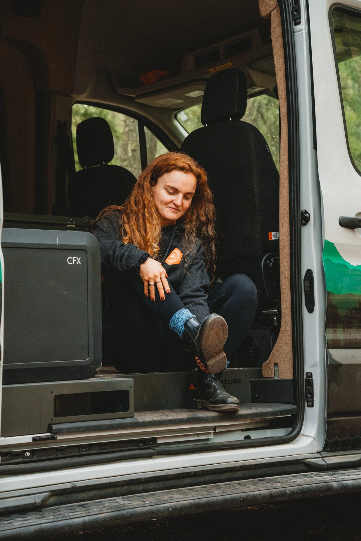 Solo traveler sitting in the open side doorway of the Adventure Wagon Solo Nomad camper van.