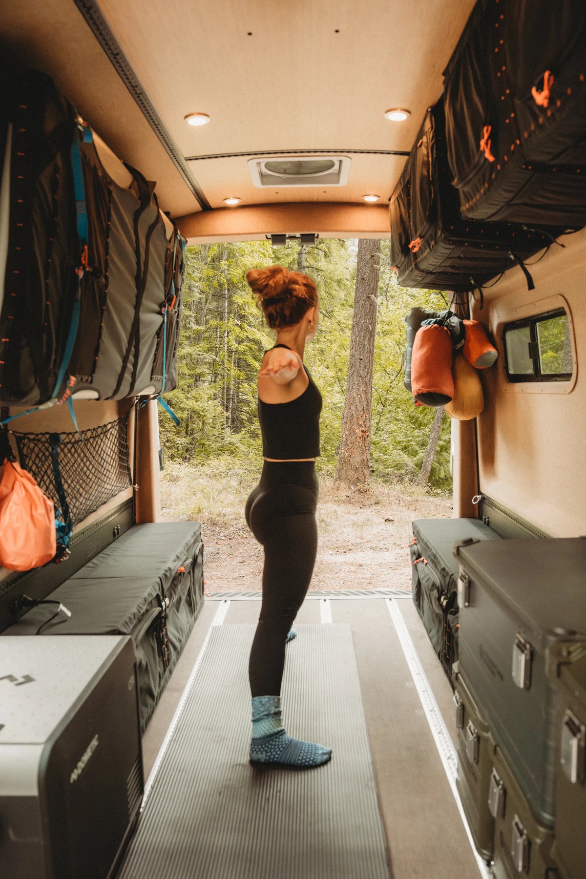 Solo traveler standing on a yoga mat inside the Adventure Wagon Solo Nomad with the rear doors open.