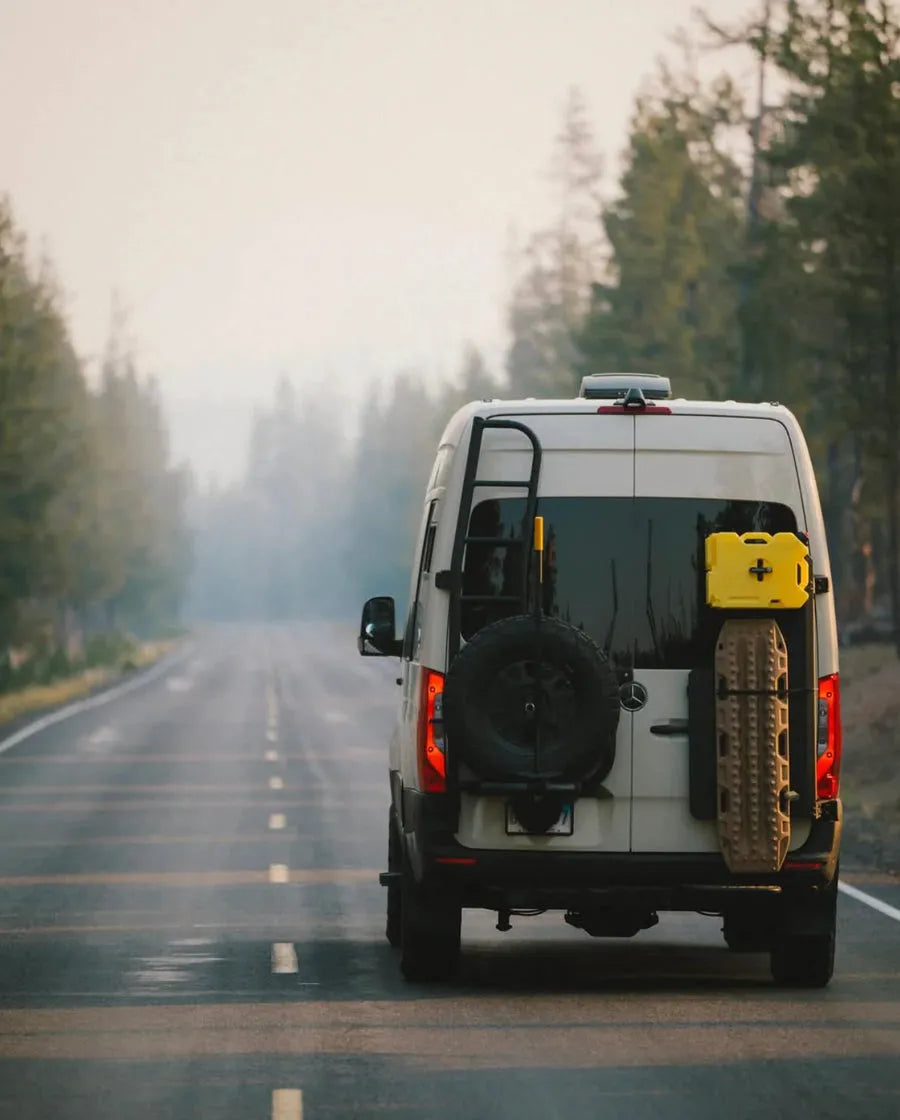 Adventure Wagon Mercedes Sprinter camper van traveling on a tree-lined forest road during an outdoor road trip.