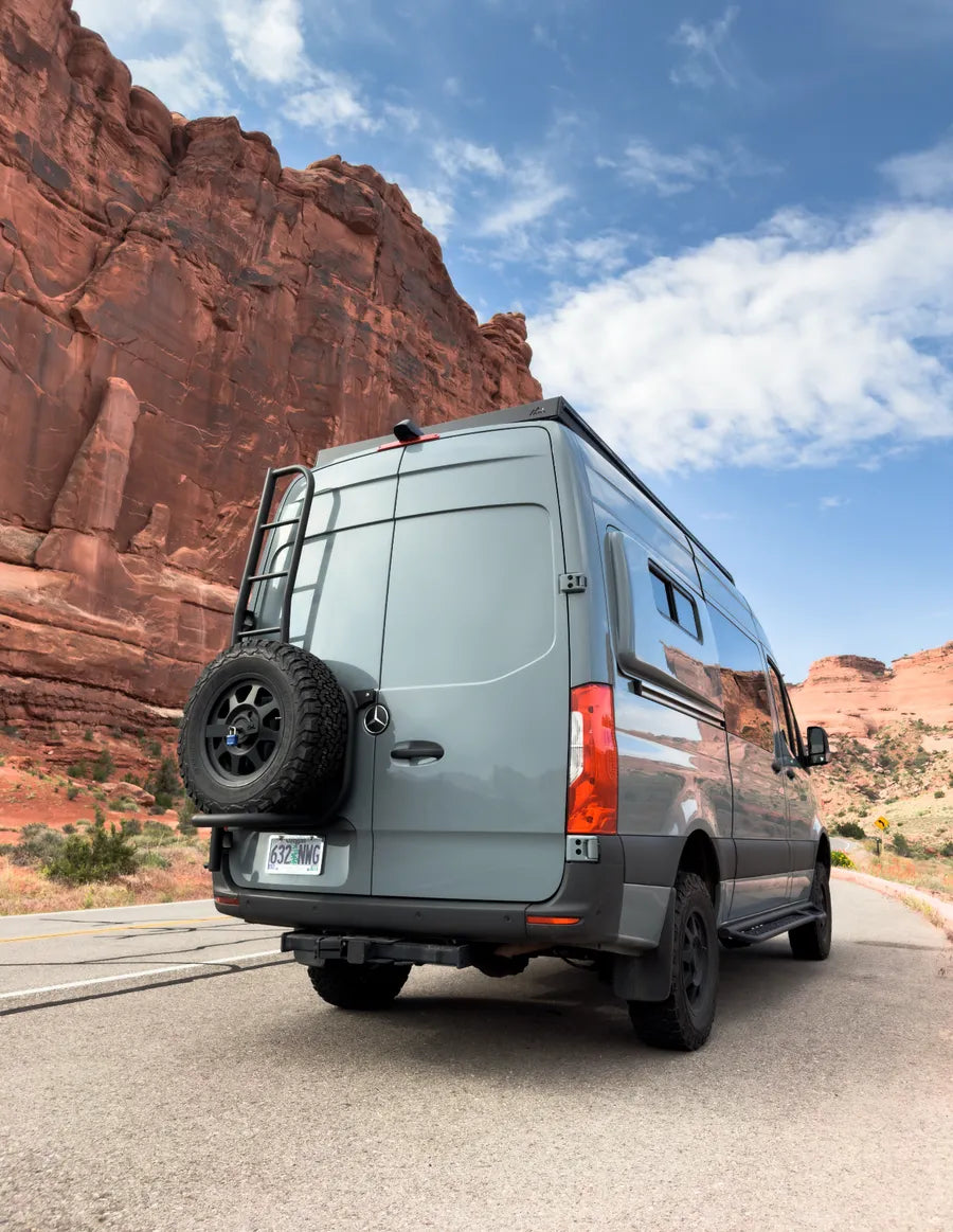 Adventure Wagon Mercedes Sprinter camper van driving through a red rock desert landscape on an unpaved road.