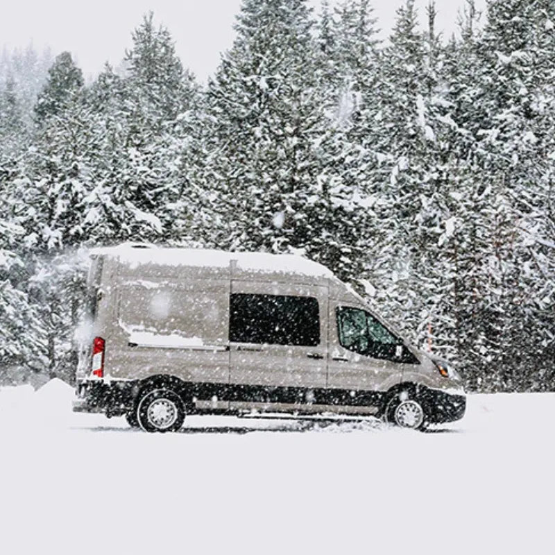 Mercedes Sprinter camper van equipped with an Adventure Wagon interior driving through deep snow in a winter forest.