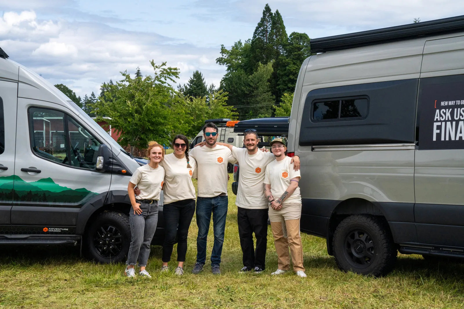 Adventure Wagon team members standing together between two custom camper vans at an outdoor van event.