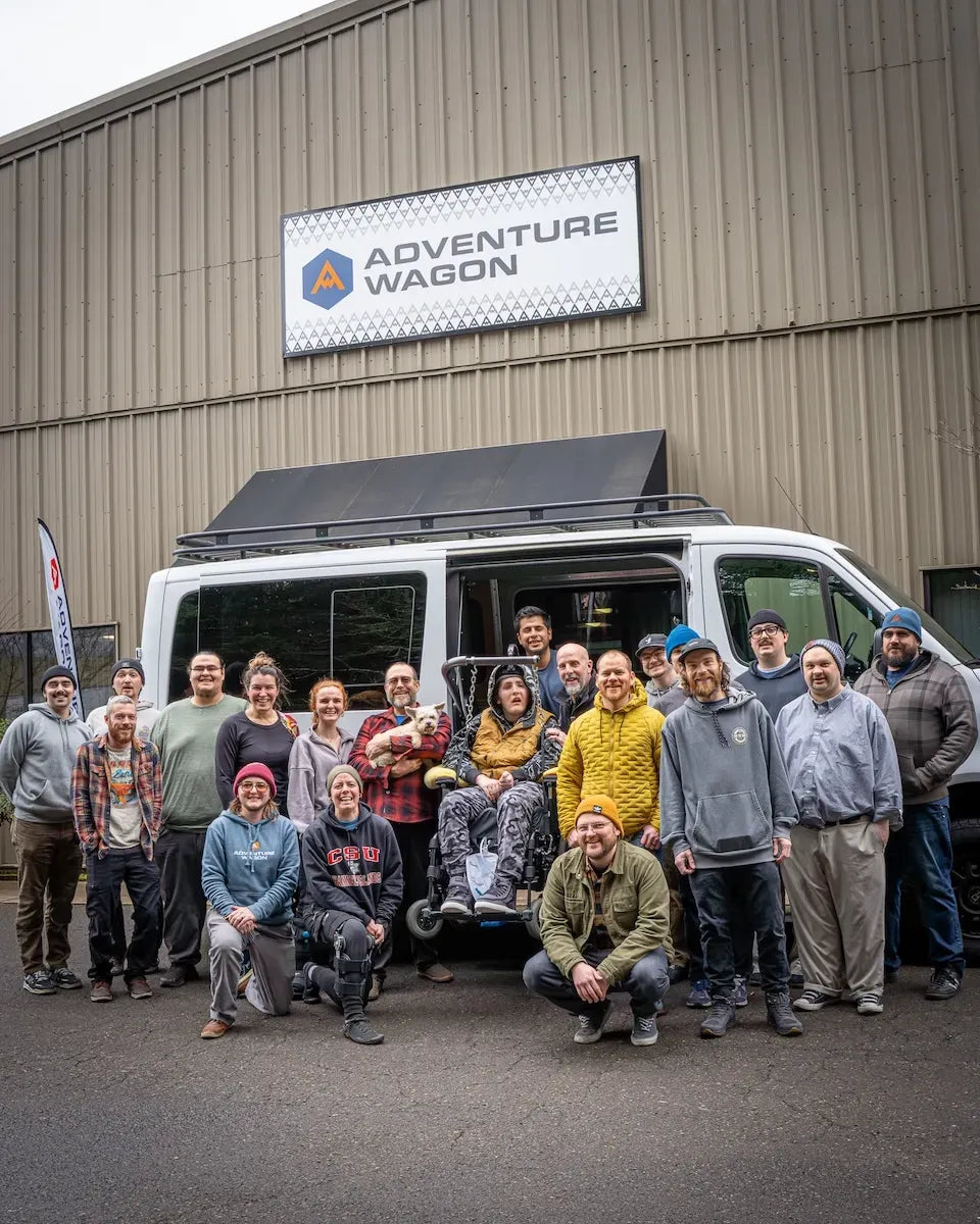 Adventure Wagon team members posing together outside the Portland factory beside a completed camper van and company signage.