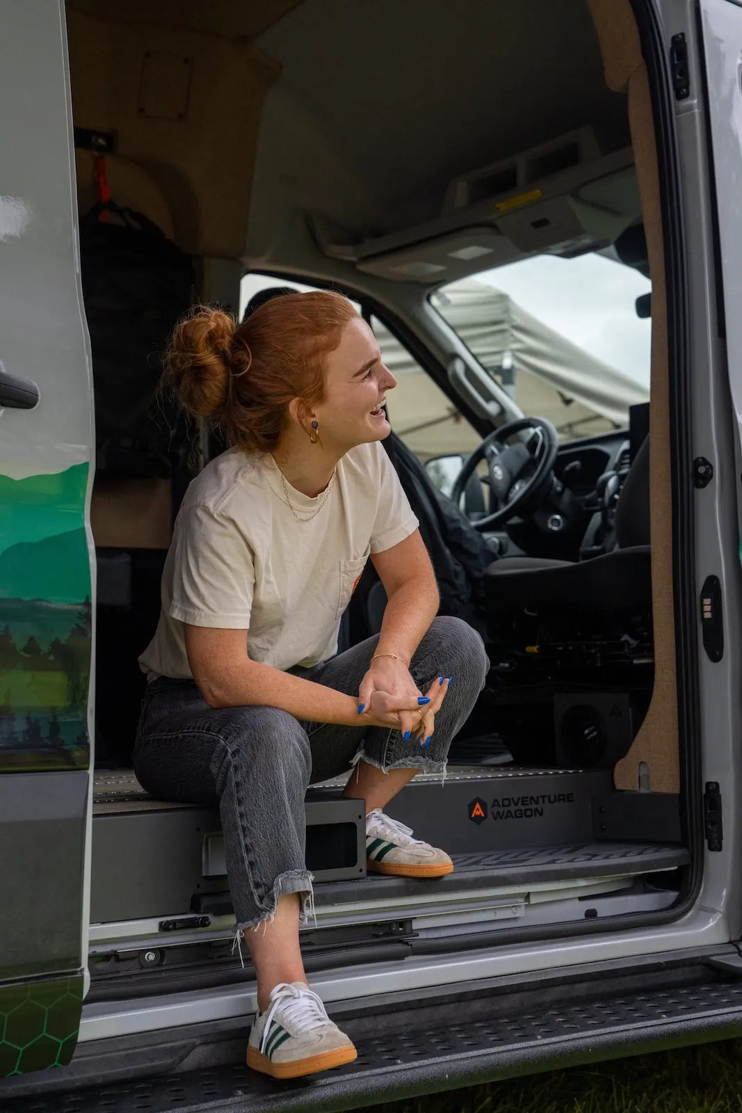 Adventure Wagon team member sitting in the open side doorway of a finished camper van with the interior and front cabin visible.